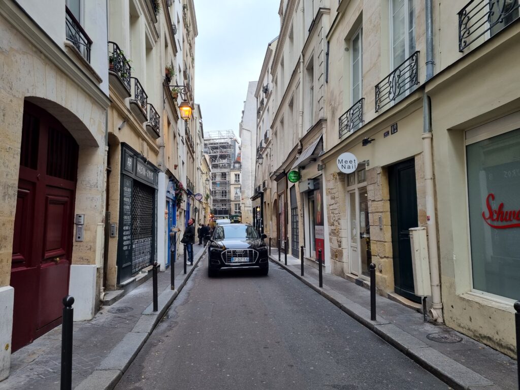 Picture of the Narrow street with a car in the middle and Jewish restaurants called rue des Ecouffes - le Marais